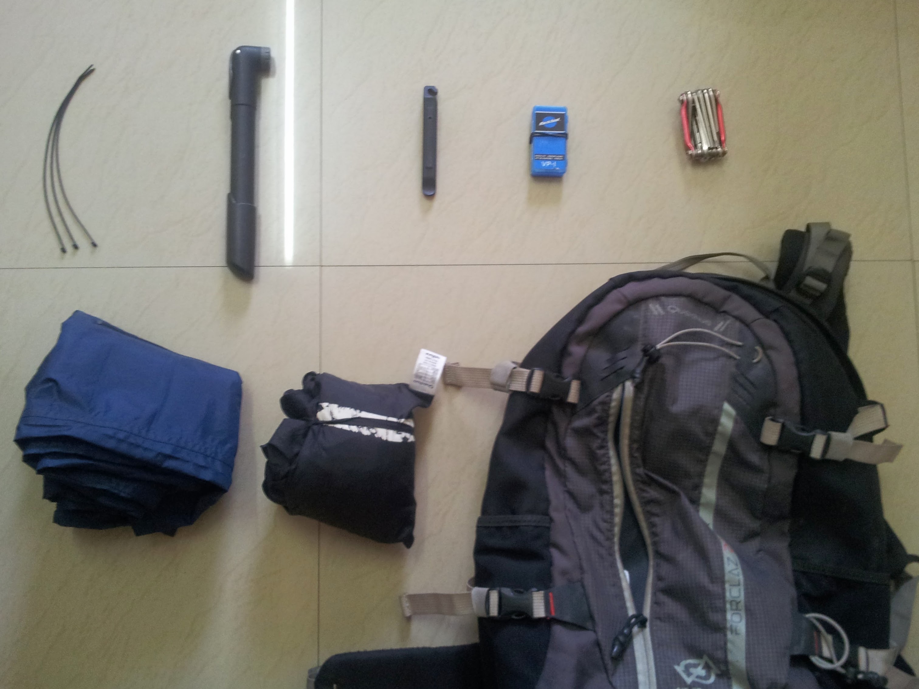 Top L-R: Cable ties, Hand pump, pair of tyre levers, Patch kit, Multitool. Bottom L-R: Rainproof lower trousers, Rainjacket, Backpack. Notice that I don&rsquo;t carry a spare tube. The commute distance is less and I have a Decathlon store nearby.