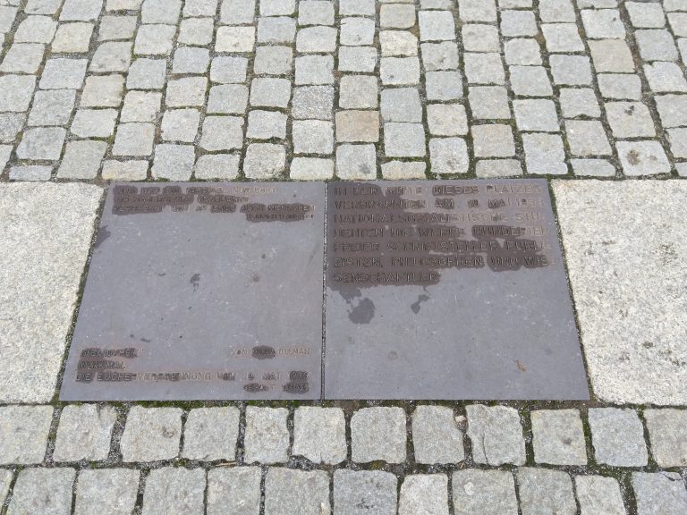 The memorial plaque for Nazi book burnings in front of Humboldt University. The memorial itself are underground empty shelves visible through a thick glass.