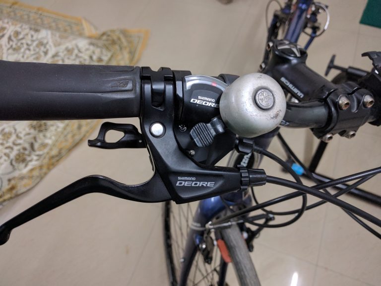 Deore Rapidfire shifters (SL-M610) and brake levers (BL-T610). The latter drives a pair of V-brakes (BR-T610). The exposed trigger in this picture is the tension releaser (shifts up for rear and down for front). These can be activated both by pushing as well as pulling. The left shifter has a lock that can restrict the front derailleur motion for a twin chainring crank.